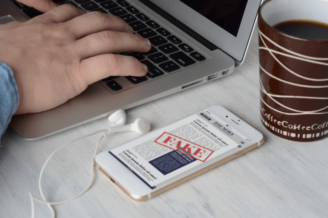 Uomo d'affari sulla tastiera con una tazza di caffè e notizie false digitali su smartphone